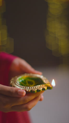 Vertical-Video-Close-Up-Of-Woman-Holding-Lit-Diya-Oil-Lamp-To-Celebrate-Festival-Of-Diwali